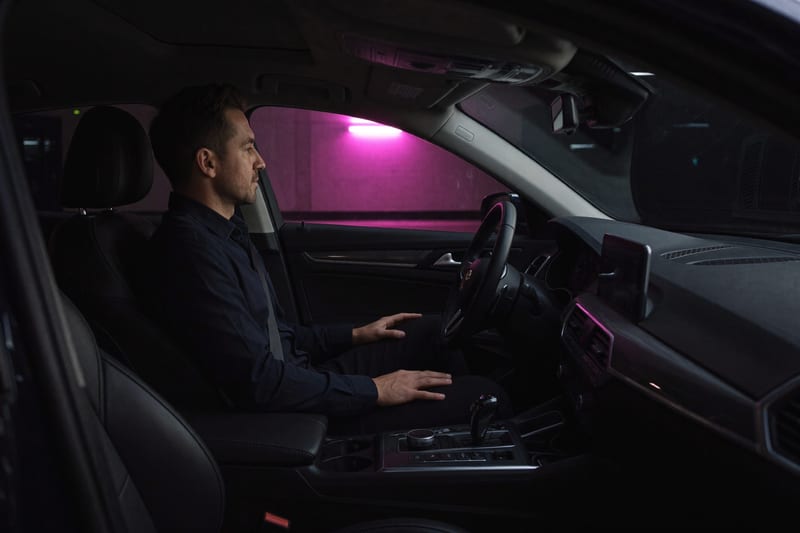 Photograph: a man sits in his parked car in a dark garage, hands at rest, dashboard unlit, waiting on a decision that is somewhere else